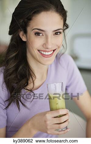 Stock Image - Woman holding a glass of cold soup and smiling. Fotosearch