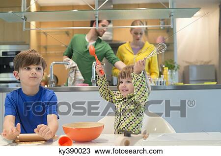 Stock Image - Children cooking in the kitchen with their parents in the background. Fotosearch