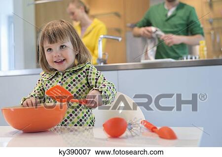 Stock Photo - Cute little girl with slotted spoon and mixing bowl in the kitchen. Fotosearch