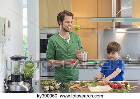 Stock Image - Man and son cutting vegetables in the kitchen. Fotosearch