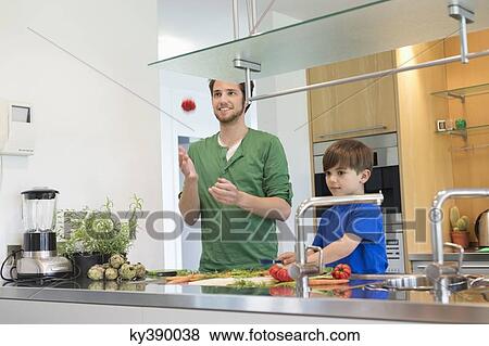 Stock Photo - Man and son cutting vegetables in the kitchen. Fotosearch