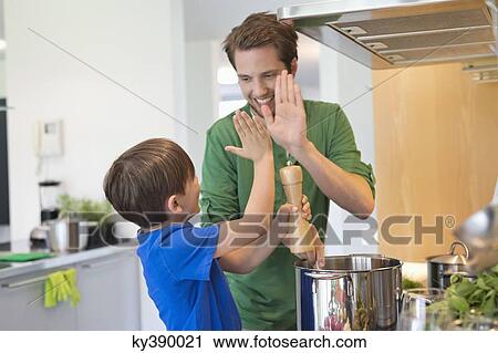 Stock Image - Man and son giving high five to each other in the kitchen. Fotosearch
