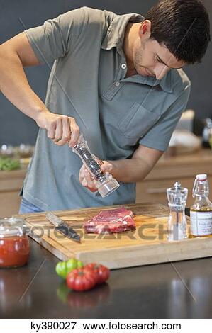 Stock Photo - Man sprinkling black pepper on the meat. Fotosearch