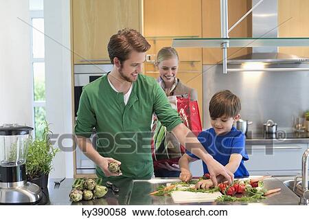 Stock Photo - Parents looking at their son cutting vegetables in the kitchen. Fotosearch