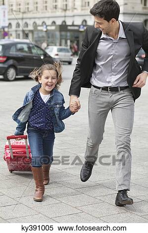 Stock Photography - Girl pulling a trolley bag while running with her father. Fotosearch