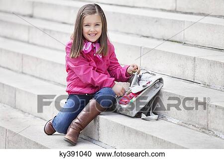 Stock Image - Portrait of a girl opening her schoolbag and smiling. Fotosearch
