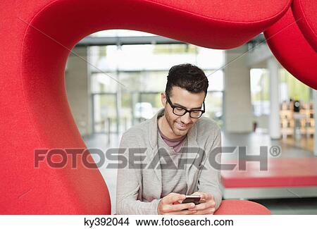 Businessman text messaging and smiling in an office View Large Photo Image Picture - Businessman text messaging and smiling in an office. Fotosearch