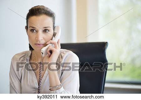 Businesswoman talking on a landline phone in an office View Large Photo Image Stock Image - Businesswoman talking on a landline phone in an office. Fotosearch