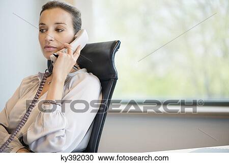Businesswoman talking on a landline phone in an office View Large Photo Image Stock Image - Businesswoman talking on a landline phone in an office. Fotosearch