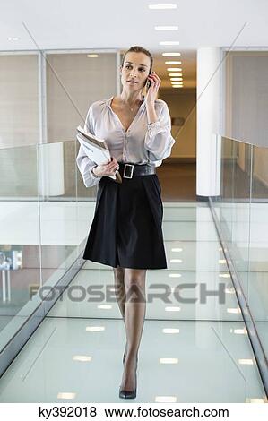 Stock Photo - Businesswoman talking on a mobile phone in an office corridor. Fotosearch