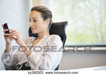 Businesswoman text messaging on a mobile phone in an office View Large Photo Image Stock Image - Businesswoman text messaging on a mobile phone in an office. Fotosearch