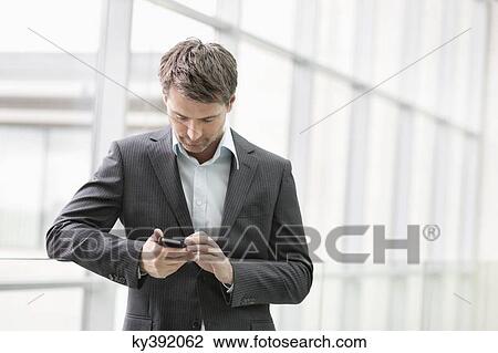 Businesswoman text messaging on a mobile phone in an office View Large Photo Image Stock Image - Businesswoman text messaging on a mobile phone in an office. Fotosearch