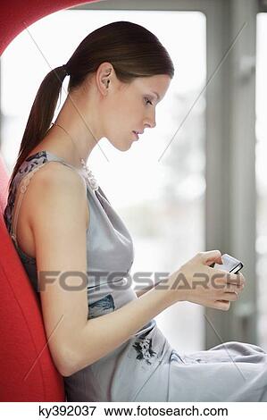 Stock Photo - Businesswoman text messaging on a mobile phone in an office. Fotosearch