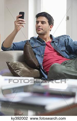 Man reclining on a couch and using a mobile phone View Large Photo Image Stock Image - Man reclining on a couch and using a mobile phone. Fotosearch