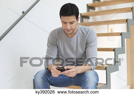 Man sitting on stairs and using a mobile phone View Large Photo Image Stock Photograph - Man sitting on stairs and using a mobile phone. Fotosearch