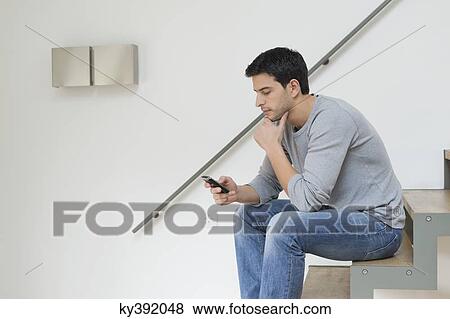 Man sitting on stairs using a mobile phone View Large Photo Image Stock Photo - Man sitting on stairs using a mobile phone. Fotosearch