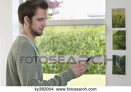 Man standing near a window using a mobile phone View Large Photo Image Picture - Man standing near a window using a mobile phone. Fotosearch