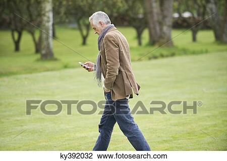 Man text messaging on a mobile phone in a park View Large Photo Image Stock Image - Man text messaging on a mobile phone in a park. Fotosearch