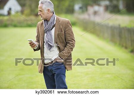 Man text messaging on a mobile phone in a lawn View Large Photo Image Stock Image - Man text messaging on a mobile phone in a lawn. Fotosearch