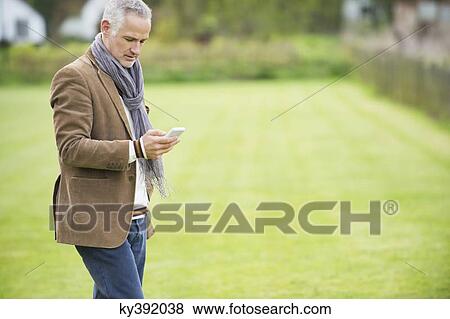 Man text messaging on a mobile phone in a park View Large Photo Image Stock Photo - Man text messaging on a mobile phone in a park. Fotosearch