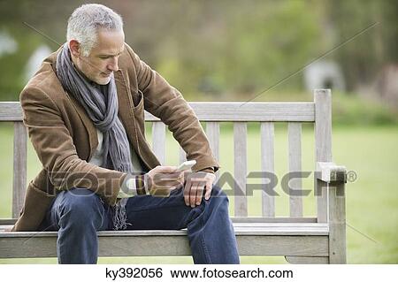 Man text messaging on a mobile phone in a park View Large Photo Image Stock Photograph - Man text messaging on a mobile phone in a park. Fotosearch