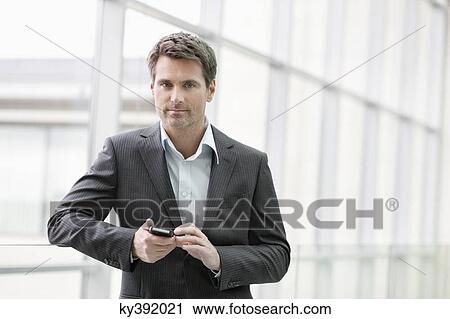 Stock Image - Portrait of a businesswoman text messaging on a mobile phone in an office. Fotosearch