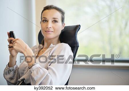 Stock Image - Portrait of a businesswoman text messaging on a mobile phone in an office. Fotosearch