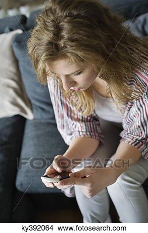 Woman text messaging on a mobile phone at home View Large Photo Image Picture - Woman text messaging on a mobile phone at home. Fotosearch