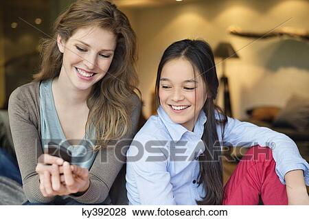 Stock Photo - Woman with her daughter using a mobile phone and smiling. Fotosearch