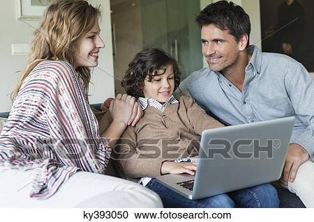Stock Image - Boy using a laptop with his parents at home. Fotosearch