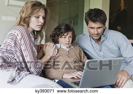 Boy using a laptop with his parents at home View Large Photo Image Stock Image - Boy using a laptop with his parents at home. Fotosearch
