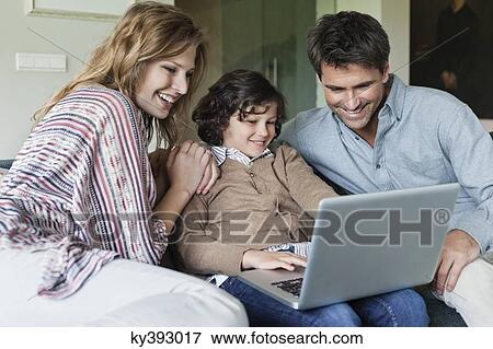 Boy using a laptop with his parents at home View Large Photo Image Stock Photo - Boy using a laptop with his parents at home. Fotosearch