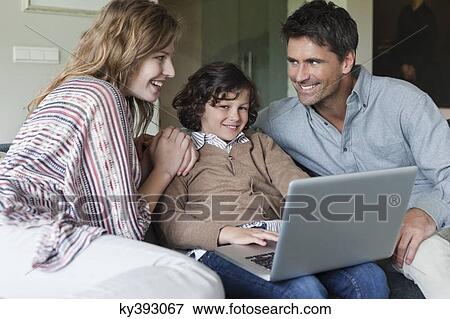 Boy using a laptop with his parents at home View Large Photo Image Stock Photo - Boy using a laptop with his parents at home. Fotosearch