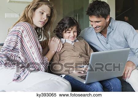 Boy using a laptop with his parents at home View Large Photo Image Stock Photography - Boy using a laptop with his parents at home. Fotosearch