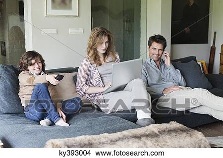 Family using electronic gadgets in a living room View Large Photo Image Picture - Family using electronic gadgets in a living room. Fotosearch