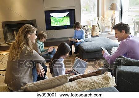 Family using electronic gadgets in a living room View Large Photo Image Stock Image - Family using electronic gadgets in a living room. Fotosearch