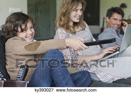 Family using electronic gadgets in a living room View Large Photo Image Stock Photo - Family using electronic gadgets in a living room. Fotosearch