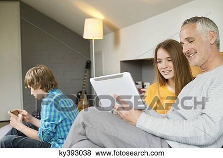 Stock Photo - Man using a digital tablet with his daughter at home. Fotosearch