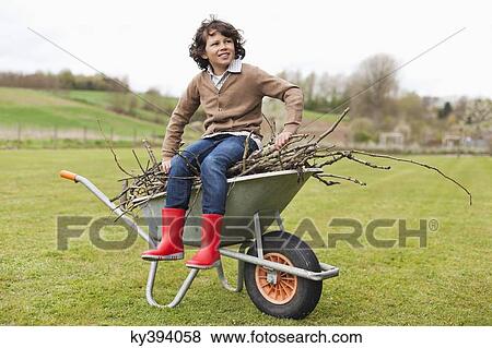 Boy sitting on a wheelbarrow with firewood in a field View Large Photo Image Stock Photo - Boy sitting on a wheelbarrow with firewood in a field. Fotosearch