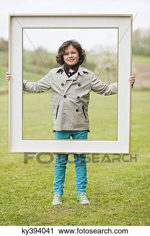 Portrait of a boy standing with a frame in a park View Large Photo Image Stock Image - Portrait of a boy standing with a frame in a park. Fotosearch