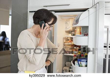 Elderly woman looking at a refrigerator and talking on a mobile phone View Large Photo Image Stock Photo - Elderly woman looking at a refrigerator and talking on a mobile phone. Fotosearch