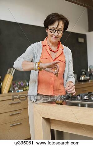 Stock Image - Elderly woman preparing herbal tea in the kitchen. Fotosearch