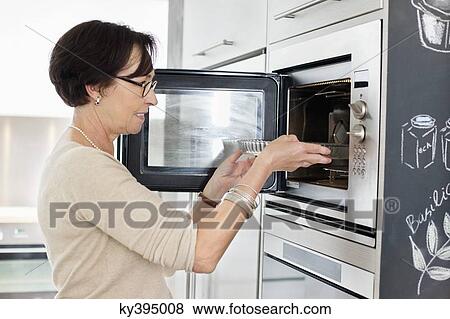 Elderly woman putting a tray into an oven View Large Photo Image Stock Photo - Elderly woman putting a tray into an oven. Fotosearch