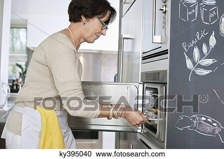 Stock Image - Elderly woman putting a tray of seafood into an oven. Fotosearch