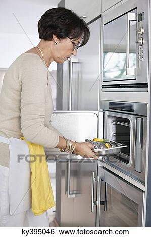 Stock Photograph - Elderly woman putting a tray of seafood into an oven. Fotosearch