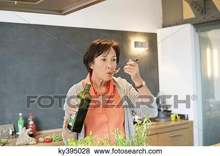 Stock Photo - Elderly woman tasting olive oil in the kitchen. Fotosearch