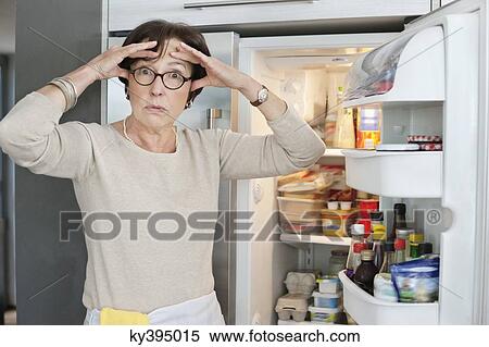 Stock Photography - Portrait of an elderly woman looking shocked in front of a refrigerator. Fotosearch