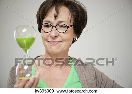 Woman looking at an hourglass and smiling View Large Photo Image Stock Photo - Woman looking at an hourglass and smiling. Fotosearch