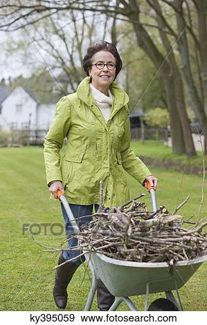 Woman pushing a wheelbarrow full of branches View Large Photo Image Stock Photo - Woman pushing a wheelbarrow full of branches. Fotosearch