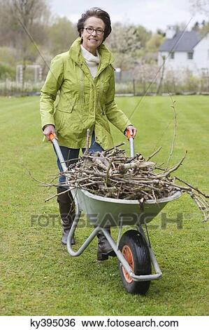 Stock Photograph - Woman pushing a wheelbarrow full of branches. Fotosearch